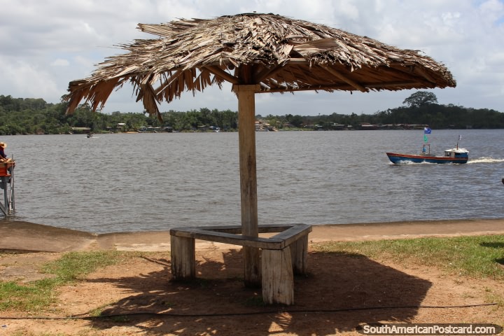 Asientos públicos bajo una sombrilla de paja en Saint Georges junto al río, en la Guayana Francesa. (720x480px). Las 3 Guayanas, Sudamerica.