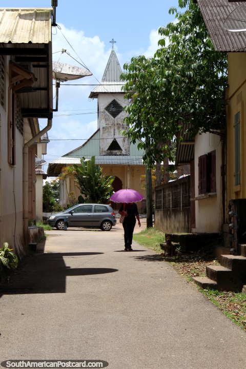 A mulher com o guarda-chuva purpúreo anda em frente da igreja no Santo Georges, Guiana Francesa. (480x720px). As 3 Guianas, América do Sul.