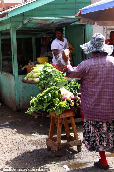 Uma mulher borrifa a gua sobre os seus verdes no Mercado Stabroek em Georgetown, Guiana. (480x720px). As 3 Guianas, Amrica do Sul.
