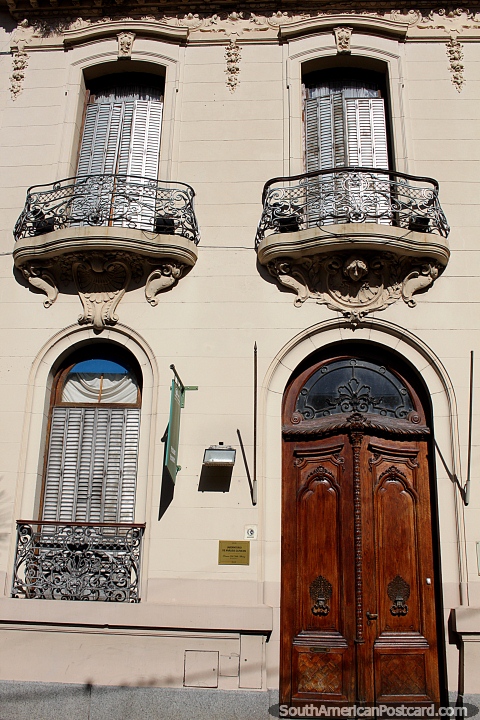 Iron balconies feature on this facade with a tall wooden door in Santa Fe. (480x720px). Argentina, South America.