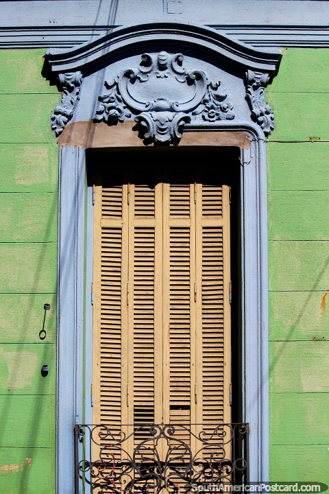 Yellow wooden window shutters surrounded by blue ceramic, a green wooden wall and black iron, house facade in Parana. (480x720px). Argentina, South America.