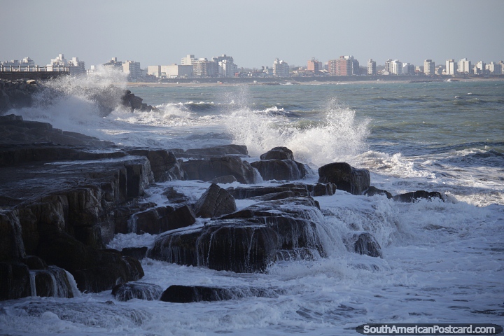 Waves crash onto the rocks on the coast in Mar del Plata, city in the distance. (720x480px). Argentina, South America.
