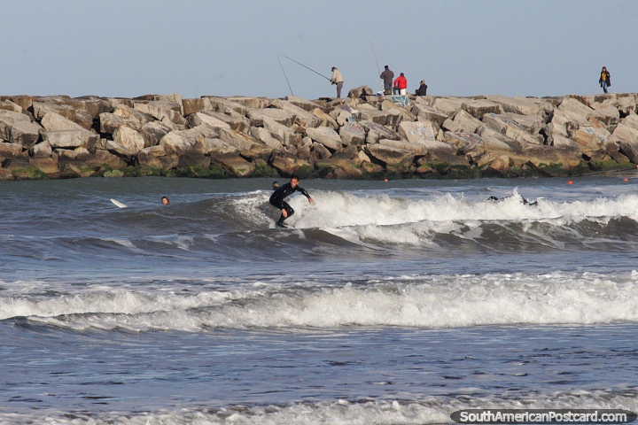 Surfing the waves at the beach in Mar del Plata with fishermen behind. (720x480px). Argentina, South America.