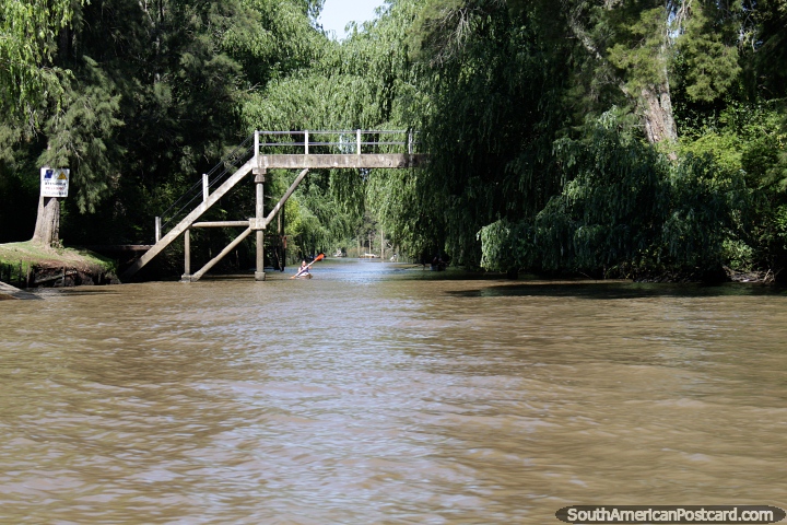 Woman in a kayak passes under a foot bridge on the river in Tigre, Buenos Aires. (720x480px). Argentina, South America.