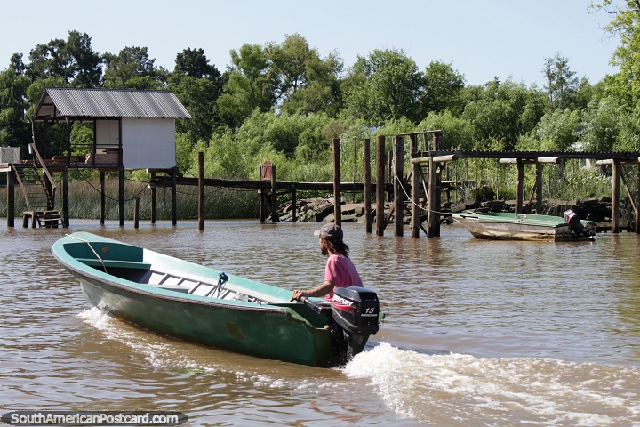 Hombre en una lancha viaja a lo largo del río pasando un embarcadero de madera en Tigre, Buenos Aires. (720x480px). Argentina, Sudamerica.