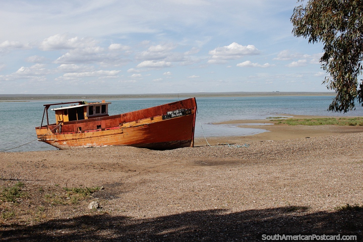 Barco de pesca de madeira laranja fica na praia na maré alta em San Antonio Oeste. (720x480px). Argentina, América do Sul.