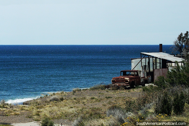 Rusty old car on the edge of a deep blue ocean north of Caleta Olivia. (720x480px). Argentina, South America.