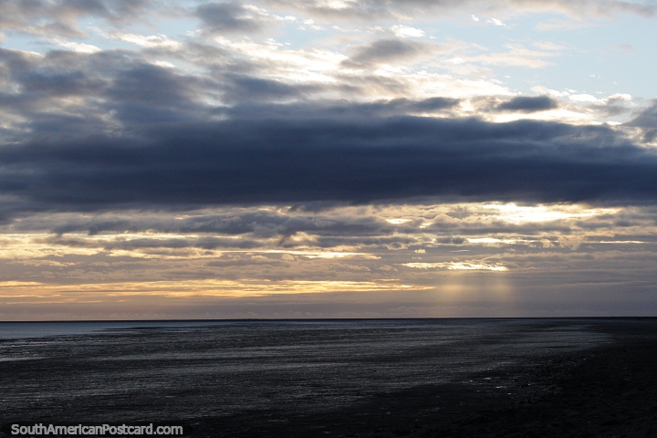 2 feixes de luz rompem as nuvens ao nascer do sol sobre o rio em Rio Gallegos. (720x480px). Argentina, Amrica do Sul.