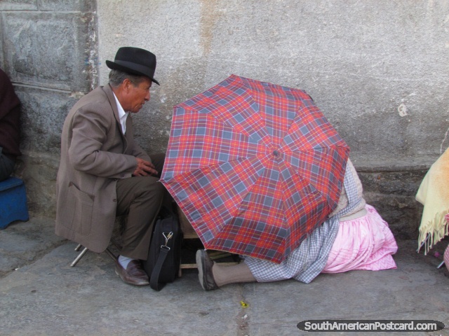 Man and woman conduct business behind an umbrella on the pavement in Oruro. (640x480px). Bolivia, South America.