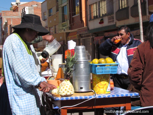 Juice stand in Desaguadero, a woman cuts pineapple and a man drinks. (640x480px). Bolivia, South America.