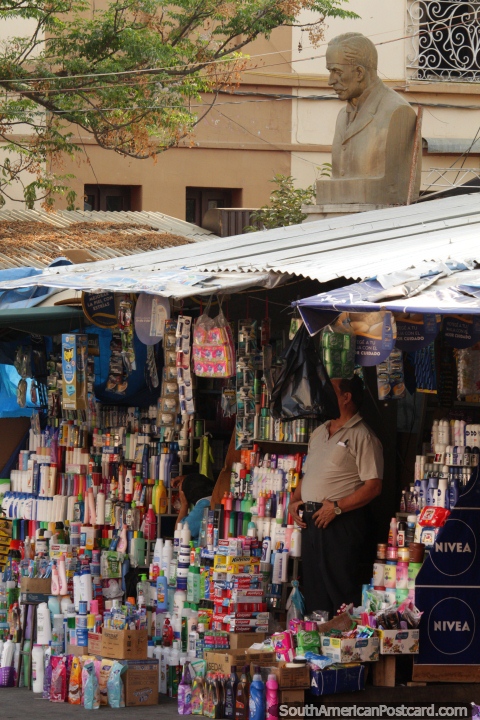 Man sells products on the street below a bust in Tarija. (480x720px). Bolivia, South America.