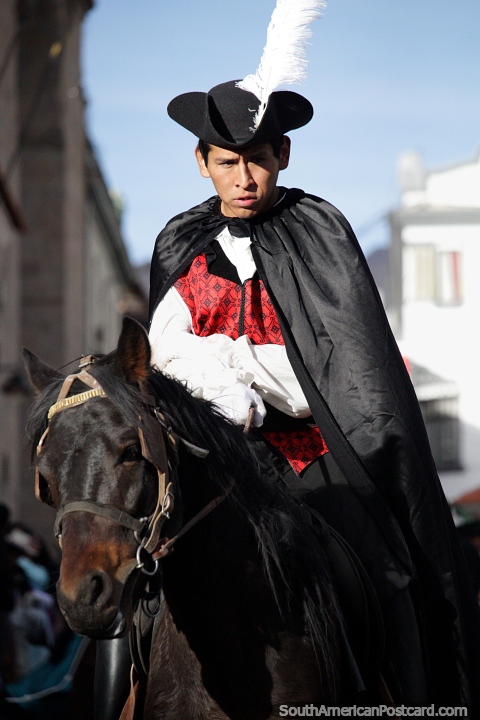 Robin Hood con plumas blancas y capa negra monta su caballo negro en Potosí. (480x720px). Bolivia, Sudamerica.