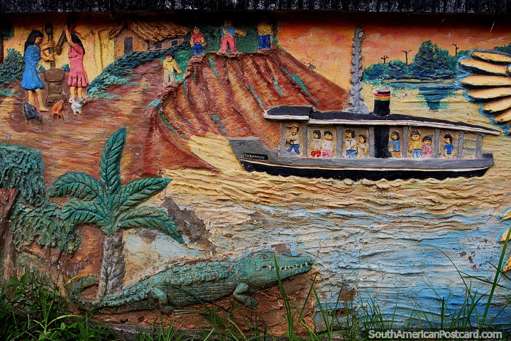 Un bote lleno de gente llega al pueblo mientras un cocodrilo se sienta en la orilla del río, un mural de concreto en la plaza en Riberalta. (720x480px). Bolivia, Sudamerica.