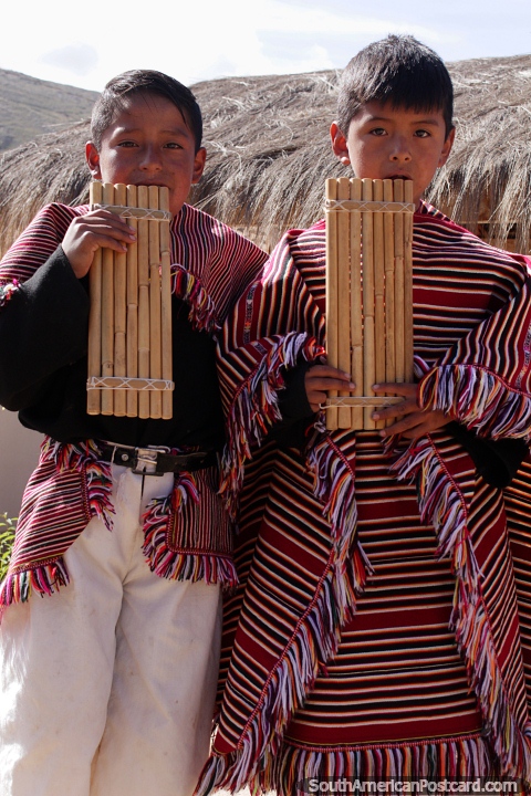 2 boys in traditional clothing blow wooden wind pipes in Puka-Puka. (480x720px). Bolivia, South America.