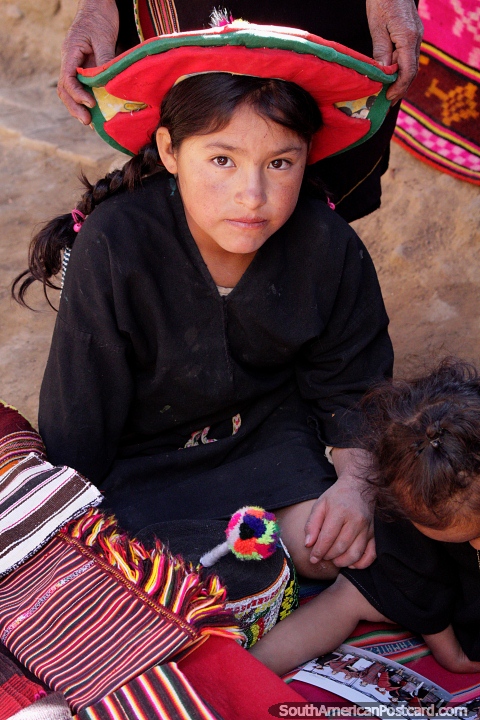 Menina jovem com chapéu vermelho, uma de várias gerações de pessoas da aldeia indïgena em Puka-Puka. (480x720px). Bolívia, América do Sul.