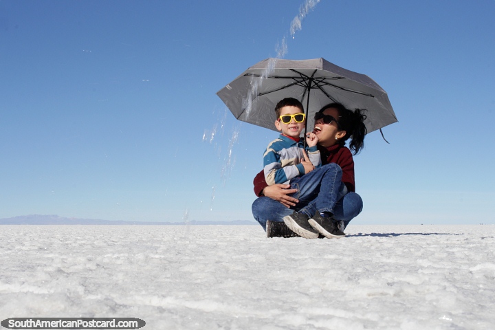 Woman and boy under an umbrella, water comes down, photo fun at the salt flats in Uyuni. (720x480px). Bolivia, South America.
