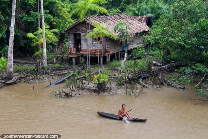 Homem em uma canoa do lado de fora de uma pequena casa de mato no Amazônia. (720x480px). Brasil, América do Sul.