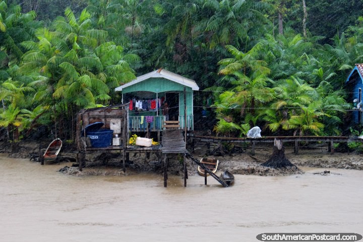 The rain falls hard in the Amazon jungle as people take shelter in their huts beside the river. (720x480px). Brazil, South America.