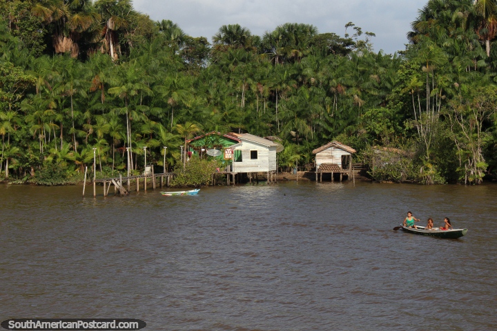 A woman and her 2 children in a canoe outside the home beside the river ...