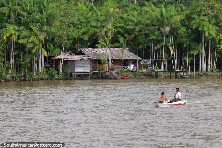 2 boys in a canoe with their house in the Amazon behind them, south of Macapa. (720x480px). Brazil, South America.