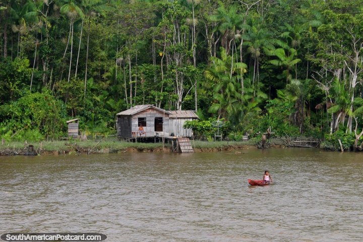 Girl in a canoe, grandfather sits outside their wooden hut in the Amazon, south of Macapa. (720x480px). Brazil, South America.