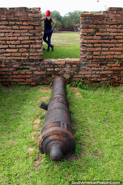 Um canhão aponta para uma menina com o cabelo ruivo tingido no forte Macapa. (480x720px). Brasil, América do Sul.