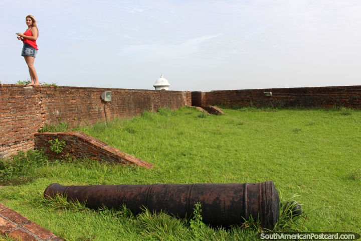 Chica en rojo en una pared de ladrillo y un cañón en la fortaleza en Macapá. (720x480px). Brasil, Sudamerica.