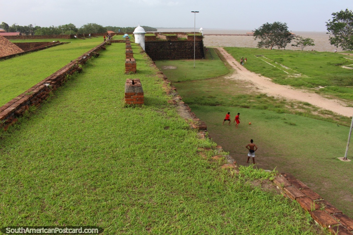 Os rapazes jogam o futebol em baixo da fortaleza junto do Rio de Amazônia em Macapa. (720x480px). Brasil, América do Sul.