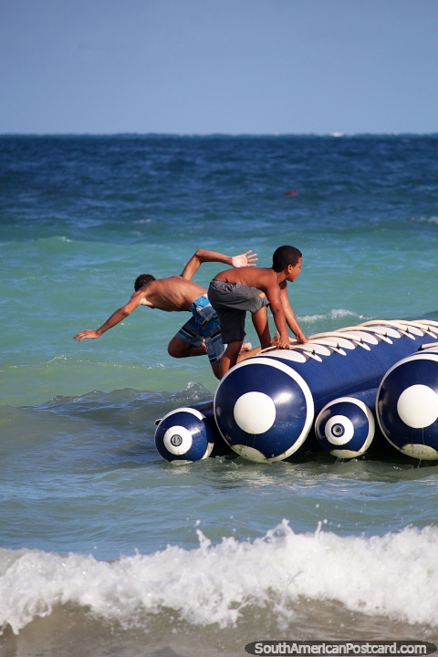 As crianças locais de Maragogi divertem-se em um Barco de Banana na praia. (480x720px). Brasil, América do Sul.