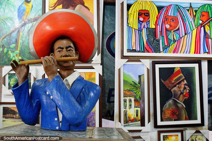 Man with orange hat plays a wooden flute, paintings behind, Olinda arts. (720x480px). Brazil, South America.
