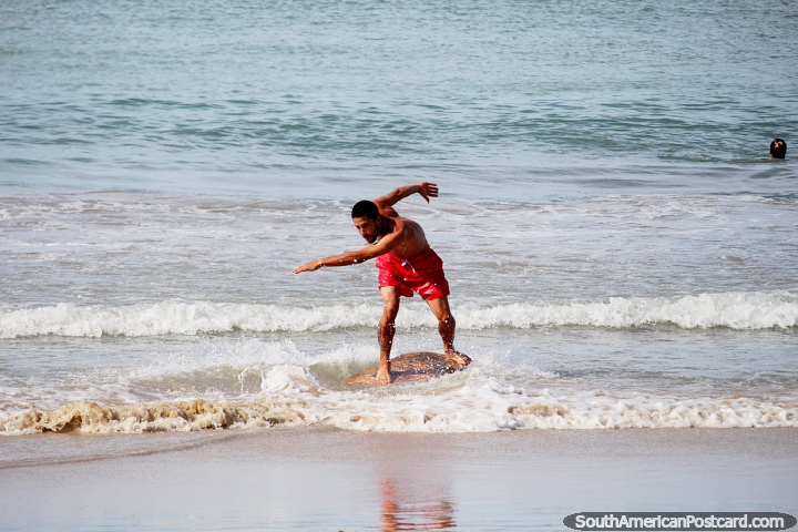 Man skates along the water on a wooden board at Dolphin Beach, Pipa. (720x480px). Brazil, South America.