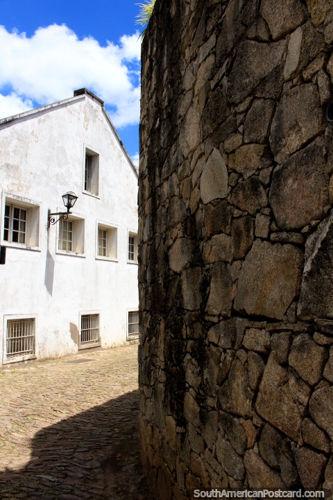 Parede de pedra no canto de uma rua de pedra arredondada e um edifïcio branco em Ouro Preto. (480x720px). Brasil, América do Sul.