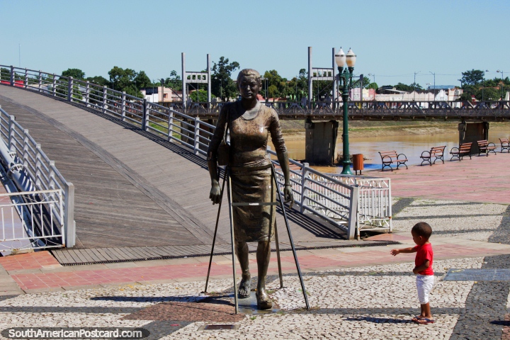 Child interacts with bronze figure of a woman in front of the bridge over the Acre River in Rio Branco. (720x480px). Brazil, South America.