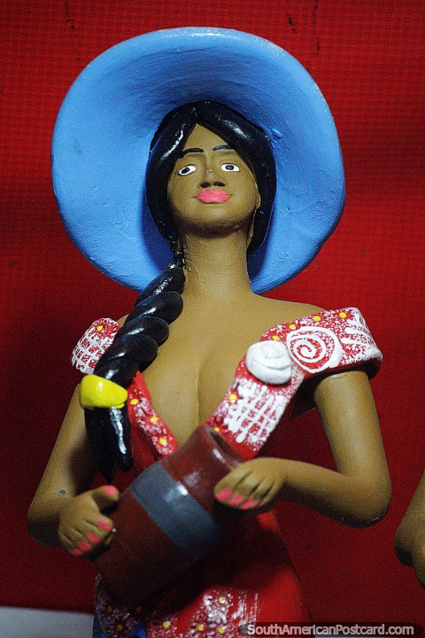 Una mujer con un gran sombrero azul sostiene una urna, una variedad de figuras en venta en Porto Velho. (480x720px). Brasil, Sudamerica.