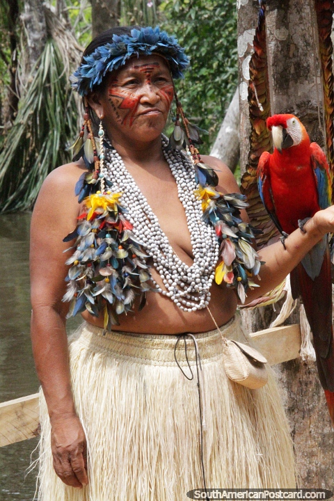 Indigenous woman dressed in traditional clothing holds a macaw, jungle in Manaus. (480x720px). Brazil, South America.