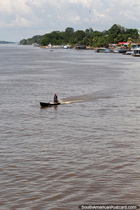 Looking upriver in a town in the Amazon, man on a small boat. (480x720px). Brazil, South America.