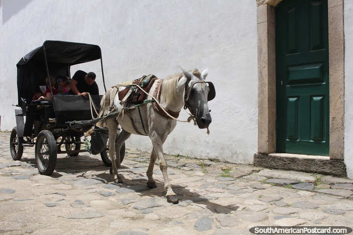 Cavalo branco puxa uma pequena carroa de passageiros pela rua de Paraty. (720x480px). Brasil, Amrica do Sul.