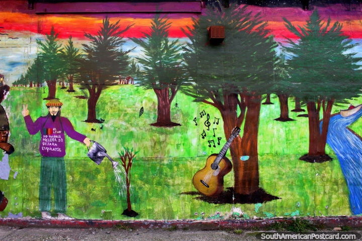 Hippie waters a tree, his guitar stands close by, river and forest, street art in Punta Arenas. (720x480px). Chile, South America.