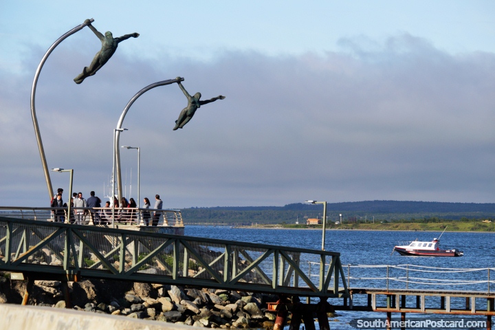Frente al mar y monumento en Puerto Natales, un par de figuras toman el cielo. (720x480px). Chile, Sudamerica.