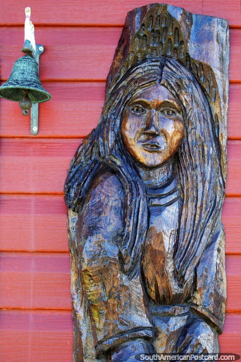 Wooden sculpture of an indigenous man and a bell in Villa Cerro Castillo. (480x720px). Chile, South America.