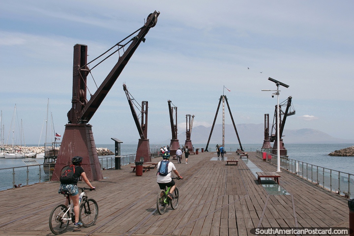 A pair ride bicycles onto the historic wharf in Antofagasta. (720x480px). Chile, South America.