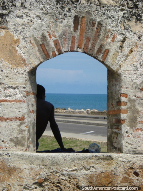 El hombre mira el mar al lado de una ventana arqueada en una pared de piedra en Cartagena. (480x640px). Colombia, Sudamerica.