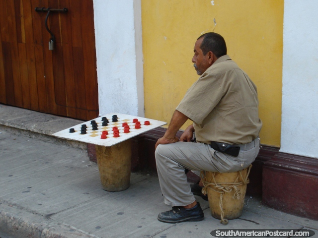 A man sits on the street waiting for a partner in a game of checkers, Cartagena. (640x480px). Colombia, South America.