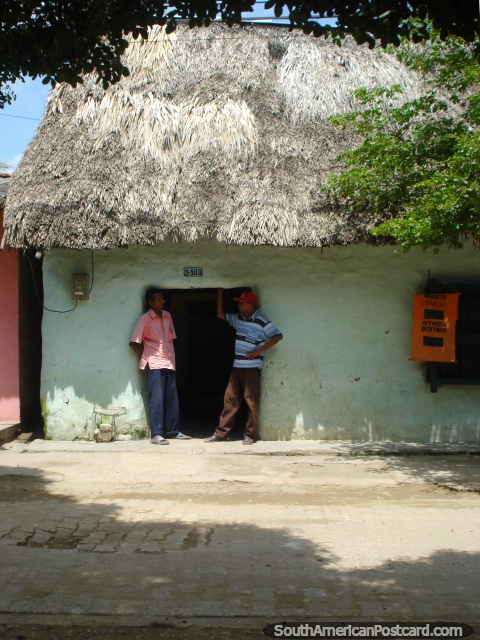 2 homens conversam na entrada de uma casa de telhado coberto com palha em Mompos. (480x640px). Colômbia, América do Sul.