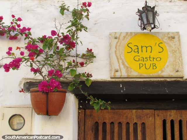 Fachada bonita do bar de Sam Gastro em San Gil, flores rosa, porta de madeira e lâmpada. (640x480px). Colômbia, América do Sul.
