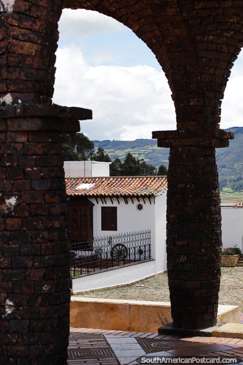 Arcos de tijolo que levam a praça pública com zona rural distante em Guatavita. (480x720px). Colômbia, América do Sul.