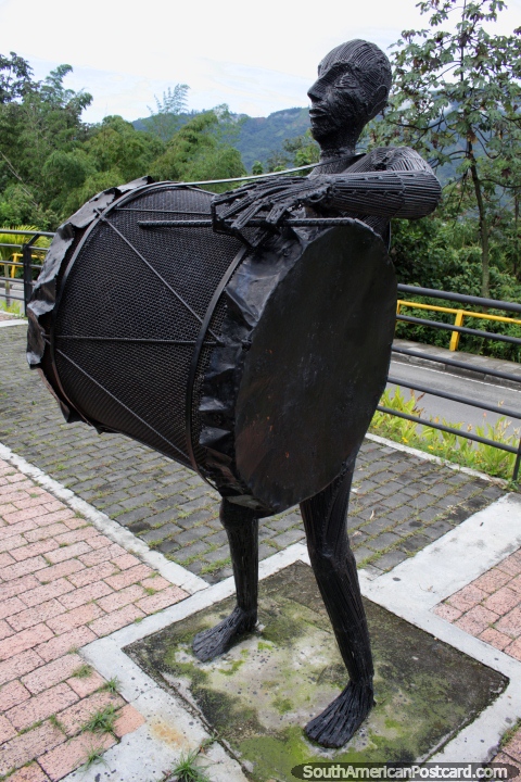O homem de ferro bate o grande tambor baixo, um de várias figuras musicais no Parque da Música em Ibague. (480x720px). Colômbia, América do Sul.
