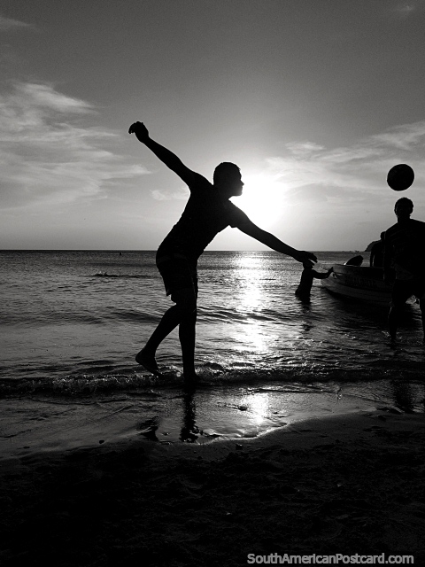 Silhouettes of boys playing soccer at the beach in Taganga at sunset, black and white. (480x640px). Colombia, South America.