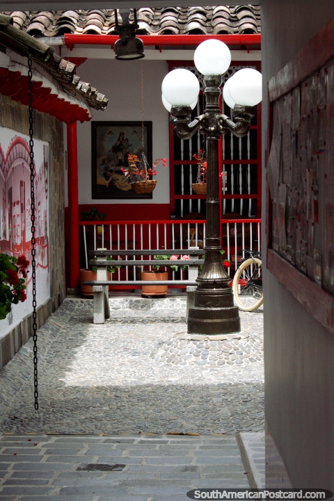 Entrada e pátio frontal do Hotel La Casona com paralelepípedos, luzes, pinturas e arte em Jardin. (480x720px). Colômbia, América do Sul.