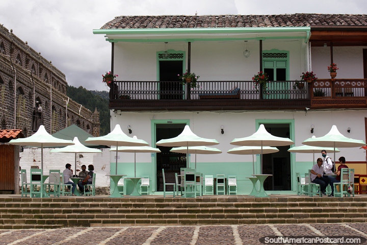 Bonito edificio que alberga una cafetera con asientos al aire libre junto a la iglesia en Jardin. (720x480px). Colombia, Sudamerica.